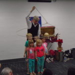 man in vest surrounded by 5 small children inside a lasso rope he is twirling