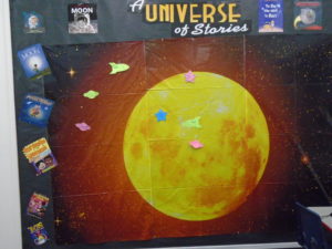 Bulletin Board background of a big yellow moon, and sign that says A Universe of Stories