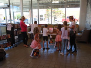 2 parents and 5 children looking at boxes of books, and various toys to choose for summer reading program prizes.