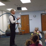 Man in vest holding hula hoop and juggling 3 balls