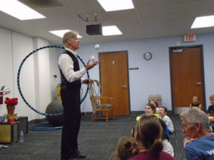 Man in vest holding hula hoop and juggling 3 balls