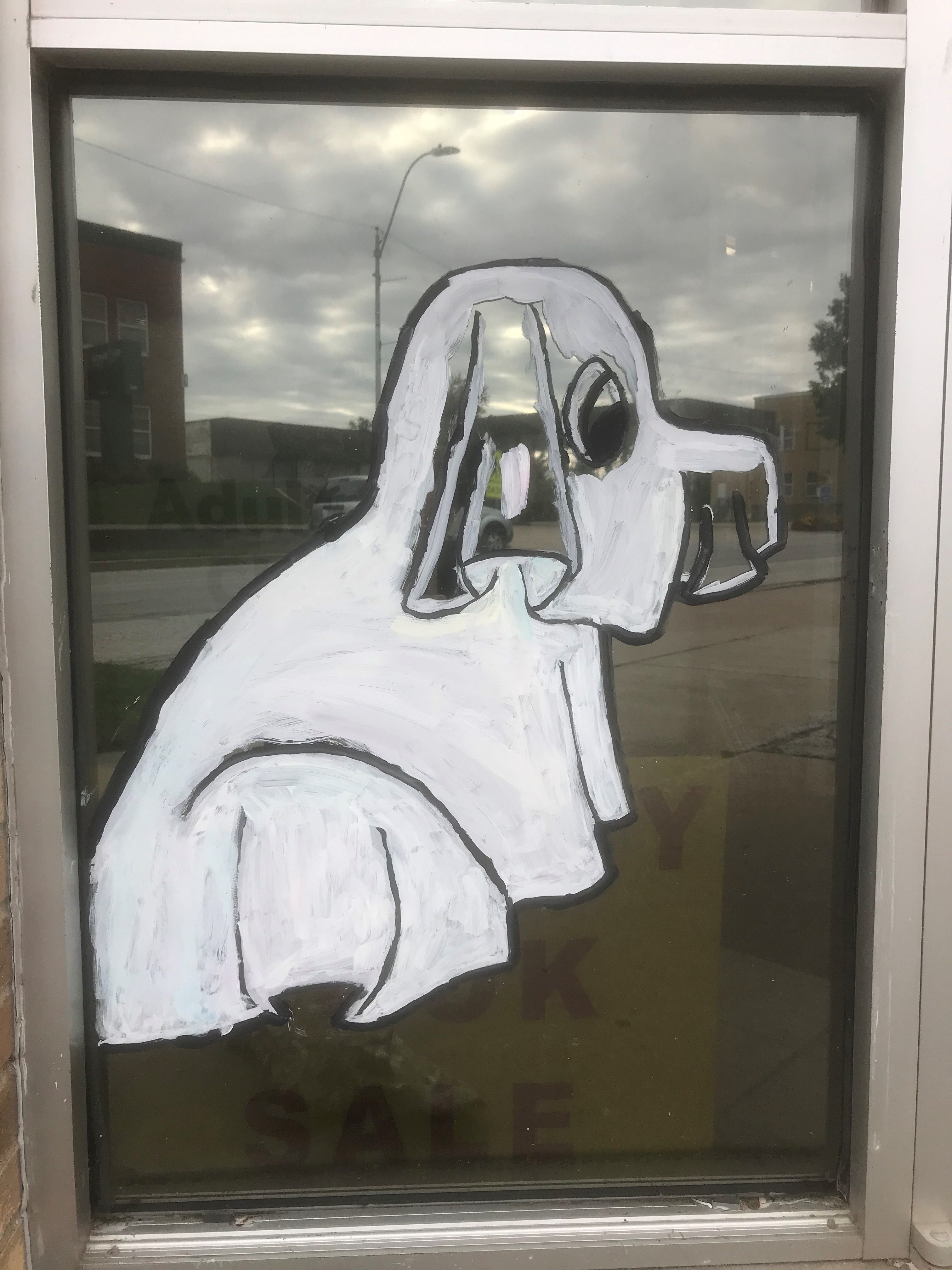 Clifford wearing a white ghost costume painted on a glass window of a building.