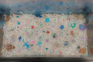 View from above of shredded white paper with small colorful objects to Seek and Find